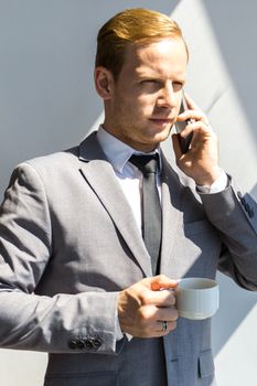 Portrait of a young business man talking on smartphone and holding cup of coffee