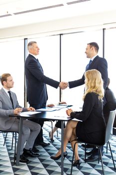 Handshake of business people at meeting in ofice , team sitting around table and discussing documents