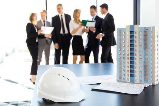 Business meeting of architects and investors, model of modern multi storey residential building house and hardhat on table , construction planning concept
