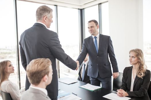 Handshake of business people at meeting in ofice , team sitting around table and discussing documents