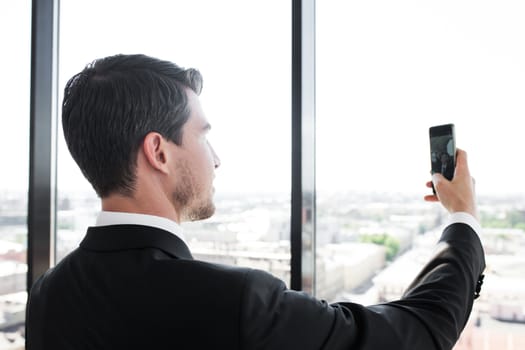 Business man in suit taking a selfie in office at panoramic window background