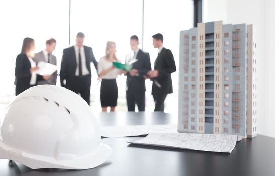 Business meeting of architects and investors, model of modern multi storey residential building house and hardhat on table , construction planning concept
