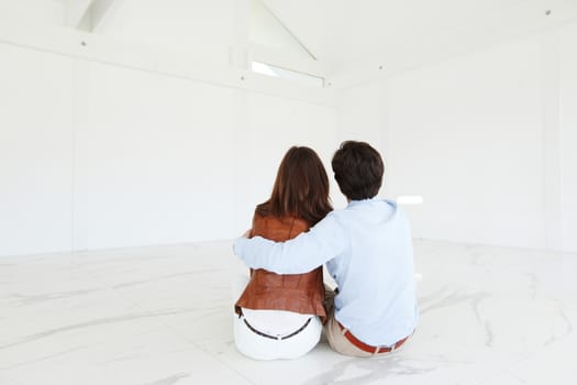 Young couple sitting on the floor of new empty house and pointing up into the air