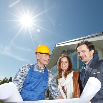 Worker shows house design plans to a young couple at construction site