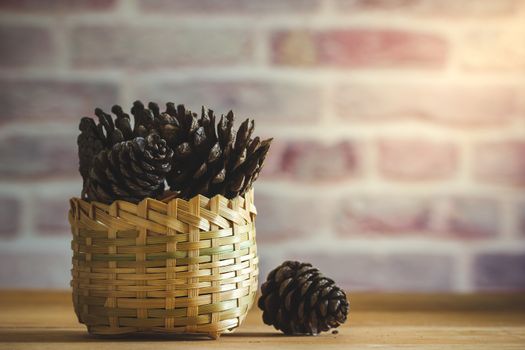 Pine Cone in bamboo basket on wooden table and brick wall background with morning sunlight.