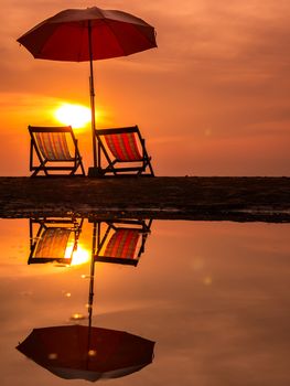 Sunrise with orange morning sky over sea with chair and umbrella on beach reflection in water, Thailand