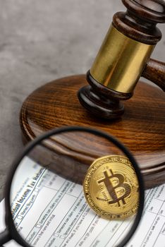 Magnifying glass with view of Bitcoin cryptocurrency in ront of gavel.Tax paying concept. 