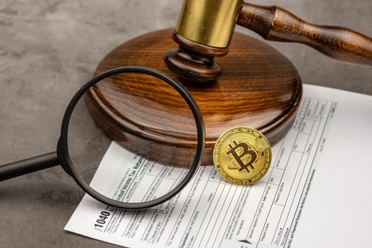 Magnifying glass with view of Bitcoin cryptocurrency in ront of gavel.Tax paying concept. 