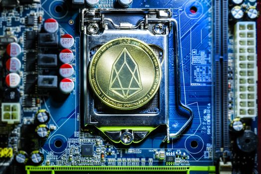 Top view of golden Eos cryptocurrency physical coin on computer mother board processor.Bitcoin mining farm, working computer equipment concept.