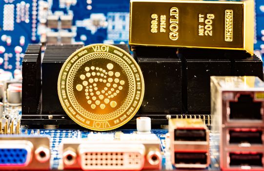 Front view of Iota cryptocurrency and golden brick or block over computer video card.Bitcoin mining farm, working computer equipment concept.
