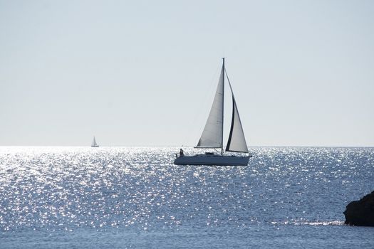 Backlit sailboat on bright and sunny sea with horizon on a winter day in Mallorca, Spain