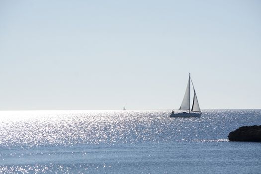 Backlit sailboat on bright and sunny sea with horizon on a winter day in Mallorca, Spain