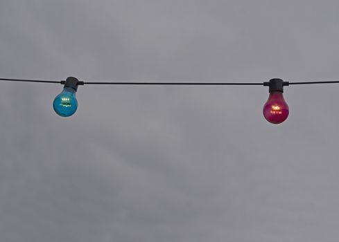 Red and blue color lightbulb on string against gray sky background