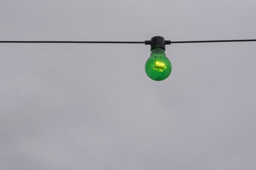 Green color lightbulb on string against gray sky background