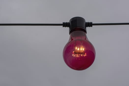 Red color lightbulb on string against gray sky background