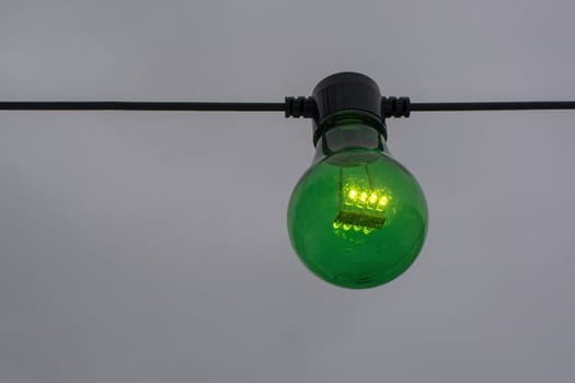 Green color lightbulb on string against gray sky background