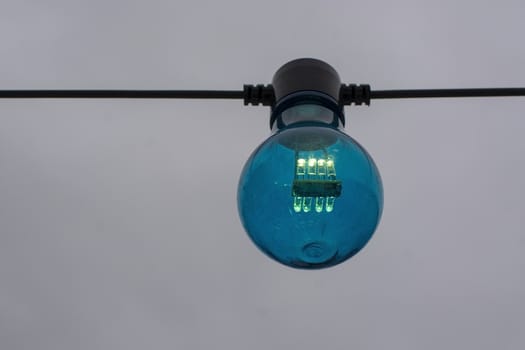 Blue color lightbulb on string against gray sky background