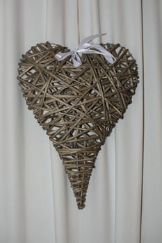 Brown rattan heart with white bow on white drape background