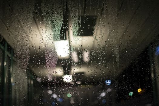 Abstract moody dew view on window with lights in commuter train transit area winter evening in Stockholm, Sweden.