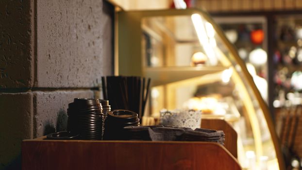 A stack of plastic caps and tubes for coffee. The self-service area in the coffee shop in brown tones - blurred background.