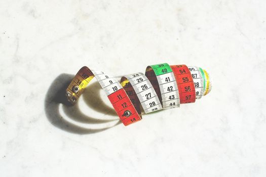 Colorful measuring tape metric system rolled up on white marble background isolated on white.