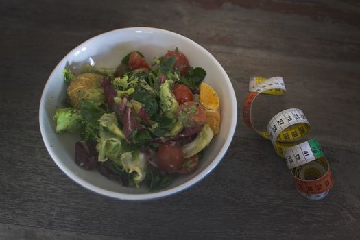 Mixed green and purple salad with measuring tape on shabby brown wooden table dieting fitness health conceptual background.