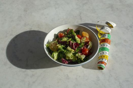 Mixed green and purple salad with measuring tape on white marble table dieting fitness health conceptual background with shadow for copy space