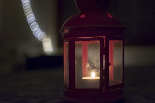 Red lantern with star on glass and burning tealight in darkness