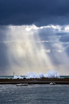 Vertical Mediterranean sea view with pier against dark skies with dramatic light on splashing waves on a winter day in Mallorca, Spain.