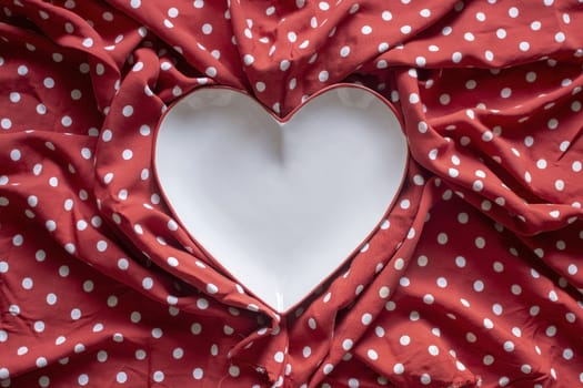 Stoneware heart shaped plate with red edge on red and white polka dot printed fabric fun romantic background texture.