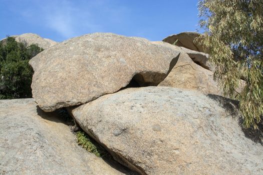 Slab of granite rock lying on top of eroded cliff with blue sky wispy cloud in Costa Smeralda, Sardinia, Italy.