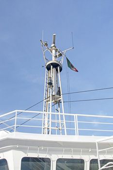 Radar technology on top of ferry boat with Italian flag variation against blue sky.