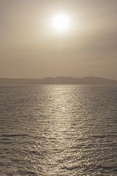 Moody seascape with sun in center and reflection on water in afternoon haze in Sardinia, Italy.