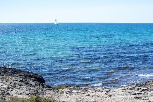 Rocky coast and sailboat on the horizon on turquoise Mediterranean sea outside Mallorca, Spain. 