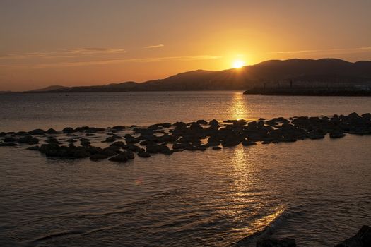 Beautiful golden sunset over mountains and ocean with string of rocks in Majorca, Spain.