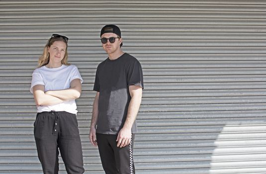 Young natural and casual sporty couple dressed man with cap backwards and woman against corrugated iron wall street style