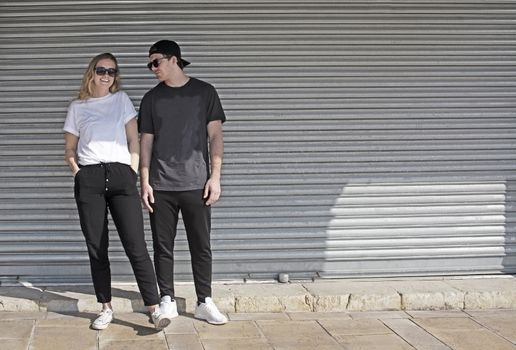 Young natural and casual sporty couple dressed man with cap backwards and woman against corrugated iron wall street style