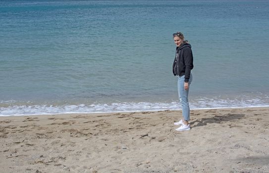 Young cute woman walks on sandy beach in spring near turquoise waterline in Mallorca Spain in March.