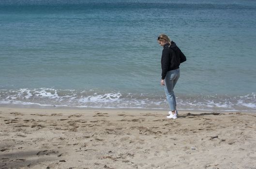 Young cute woman walks on sandy beach in spring near turquoise waterline in Mallorca Spain in March.