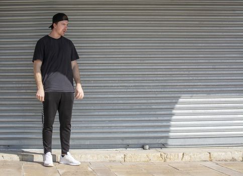 Young casual sporty dressed man with cap backwards in black against corrugated iron wall street style