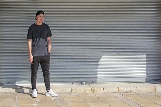 Young casual sporty dressed man with cap backwards in black against corrugated iron wall street style