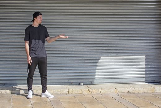 Young casual sporty dressed man with cap backwards in black against corrugated iron wall street style