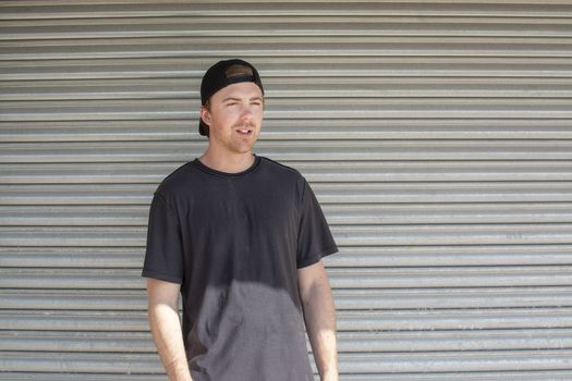 Young casual sporty dressed man with cap backwards in black against corrugated iron wall street style