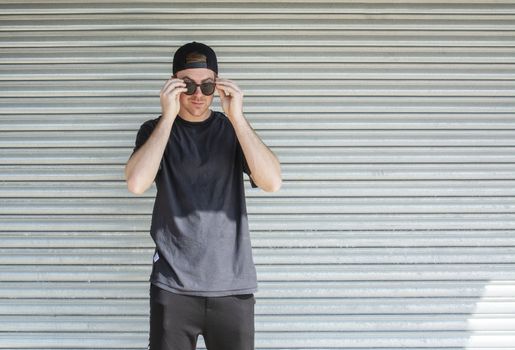 Young casual sporty dressed man with cap backwards in black against corrugated iron wall street style