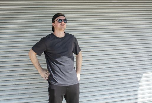 Young casual sporty dressed man with cap backwards in black against corrugated iron wall street style