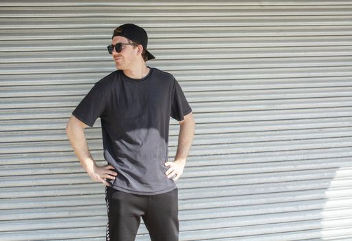 Young casual sporty dressed man with cap backwards in black against corrugated iron wall street style