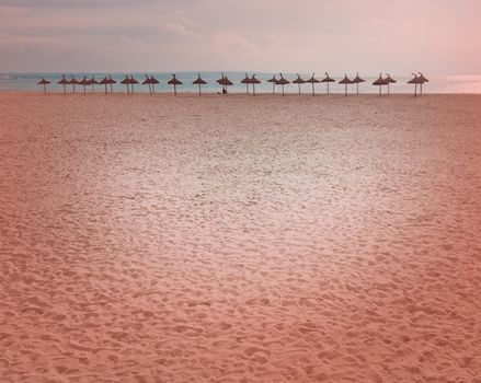 Parasols on vast empty winter beach with heart shaped spotlight background toned in color Living Coral.