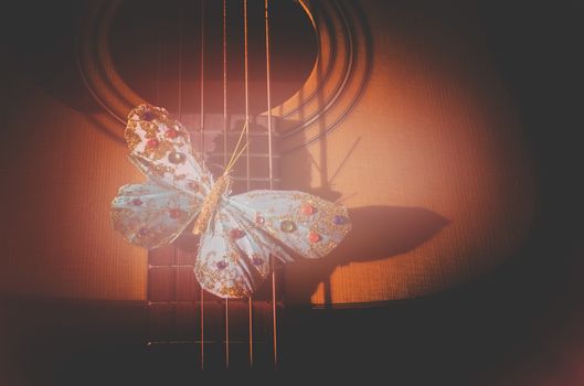 Turquoise butterfly on strings of acoustic guitar, concept for poetry, musicality, singer songwriter creativity,  toned in Living Coral warm red shades