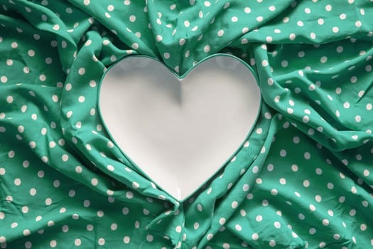 Stoneware heart shaped plate with emerald green edge on green and white polka dot printed fabric fun romantic background texture.