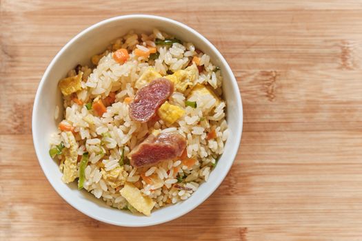 A bowl of Chinese fried rice with pork sausages and chopped vegetables.